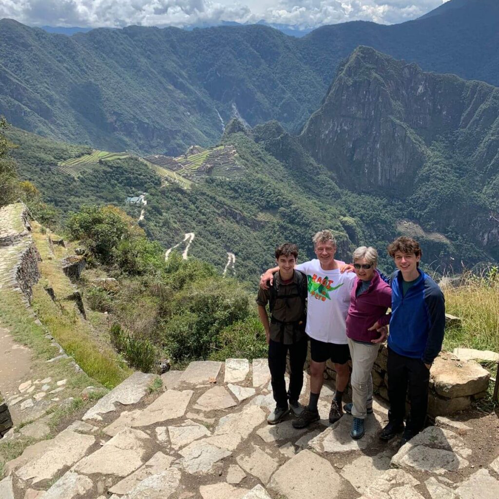 Family hiking above Machu Picchu with panoramic views of the Andes mountains and valley below.