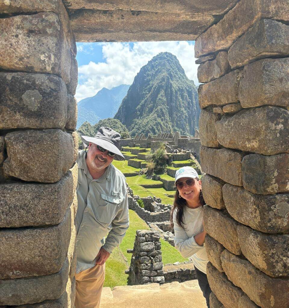 Visitors looking through an Inca stone window at Machu Picchu ruins and mountain landscape on a Machu Picchu day trip from Cusco.