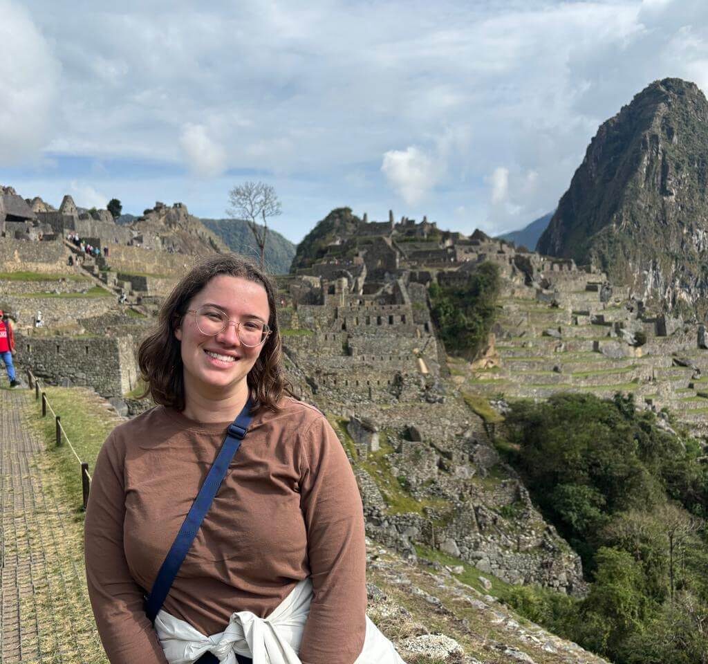 Traveler smiling with Machu Picchu terraces and stone structures in background during a Machu Picchu day trip from Cusco.