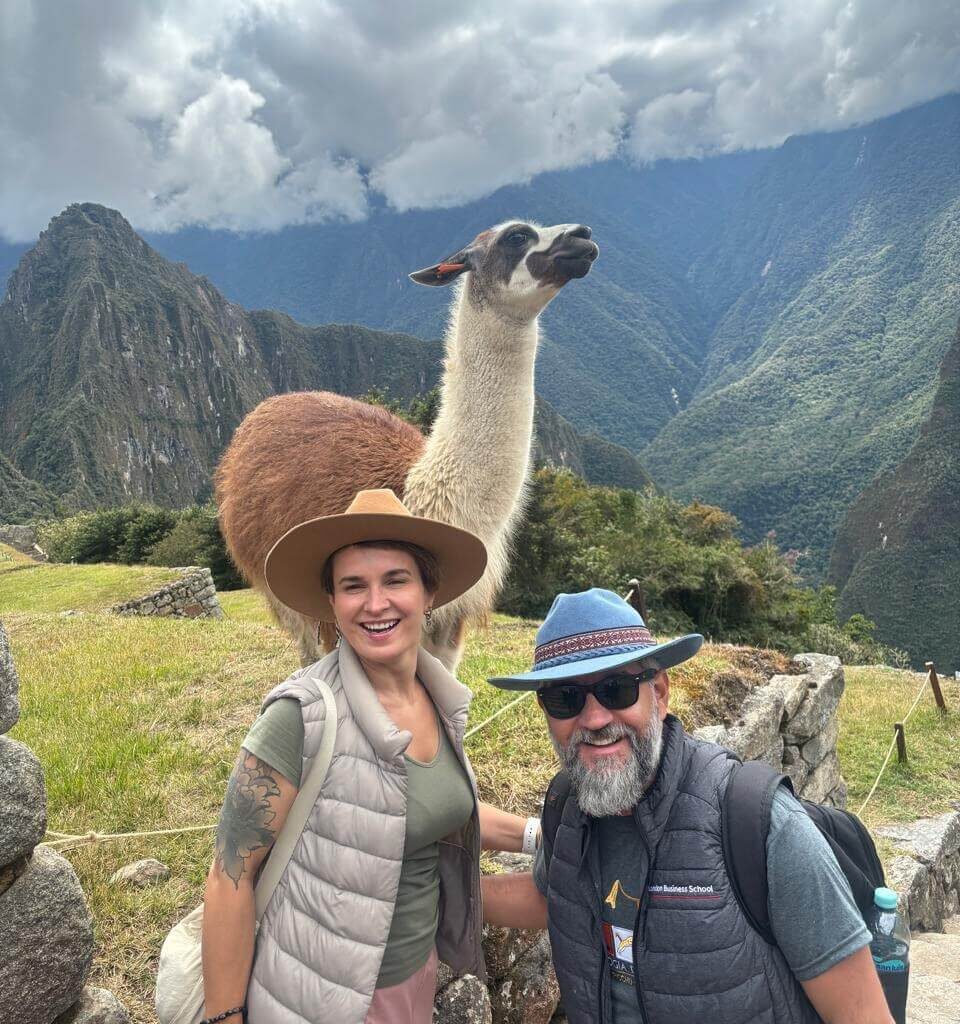 Tourists posing with a llama and Machu Picchu mountains behind on a Machu Picchu day tour from Cusco.