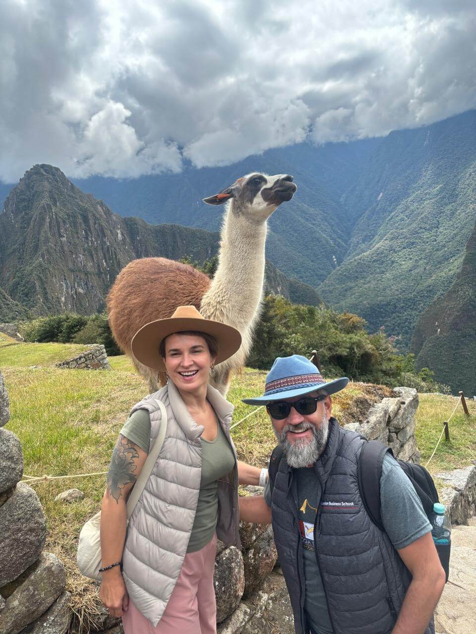 Tourists posing with a llama and Machu Picchu mountains behind on a Machu Picchu day tour from Cusco.