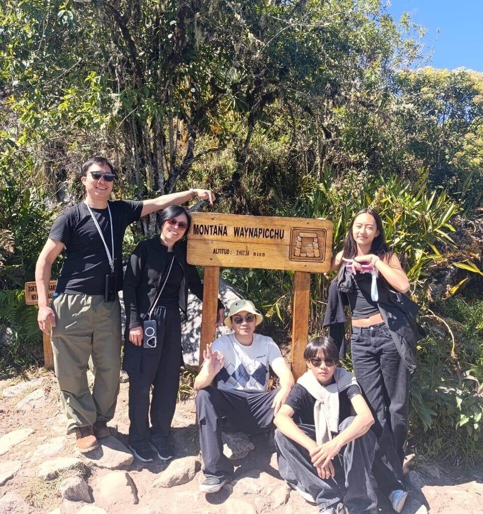 Tourists posing at Waynapicchu mountain sign inside Machu Picchu sanctuary during a Machu Picchu day tour from Cusco.