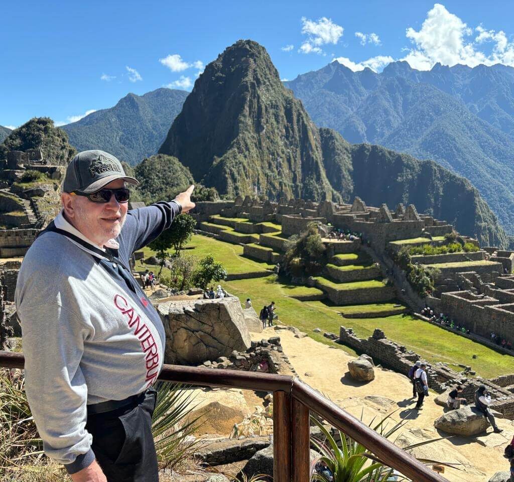 Traveler pointing toward Machu Picchu stone terraces and ruins from viewing platform with Huayna Picchu mountain behind.
