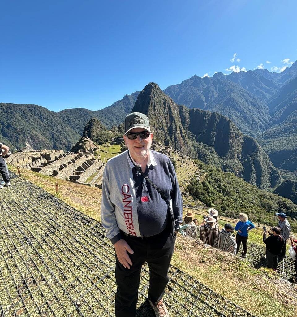 Traveler standing on viewing platform overlooking Machu Picchu ruins and mountains during sunny July weather.