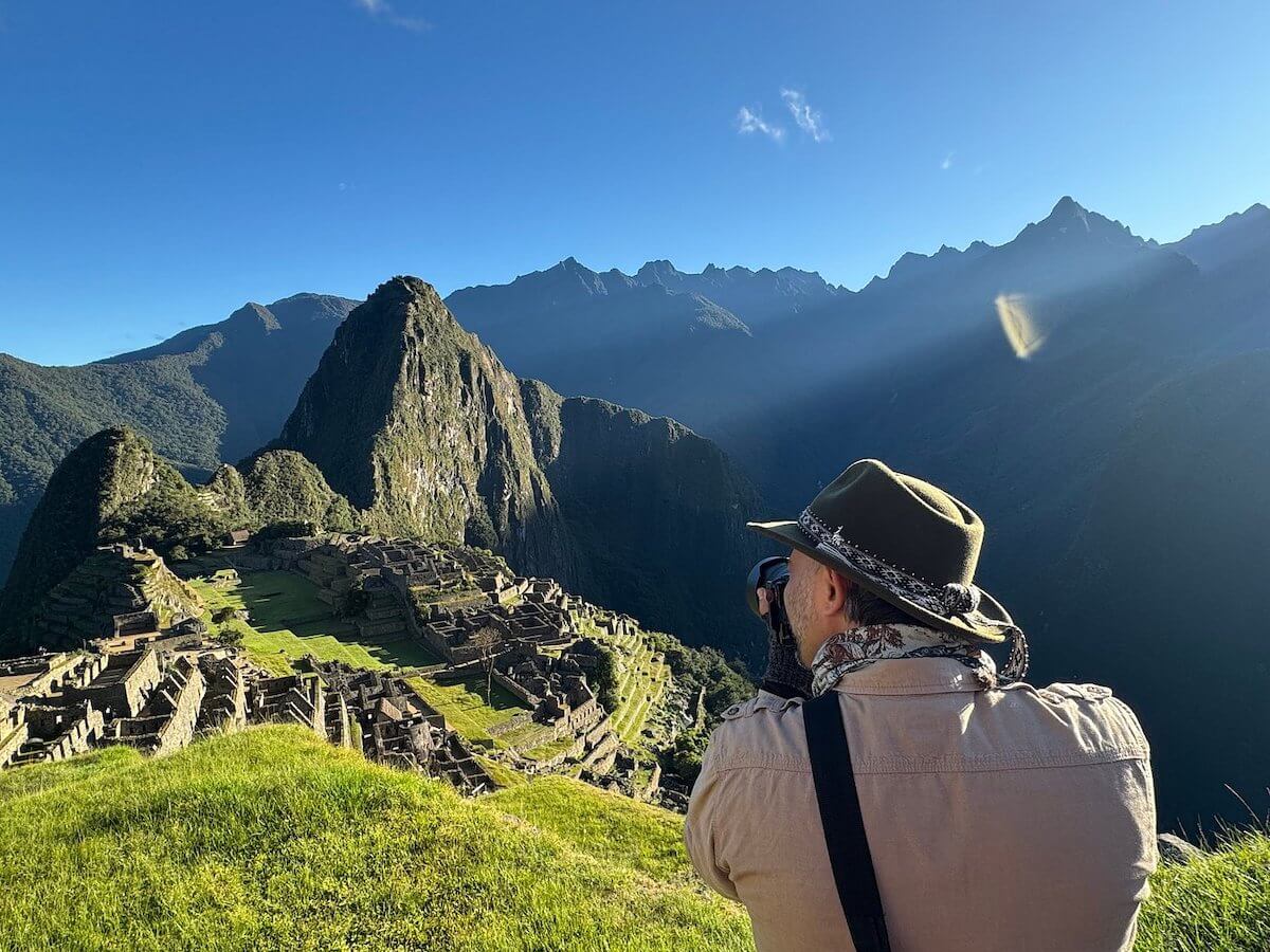 Tourist photographing Machu Picchu in June under clear blue skies with mountain views