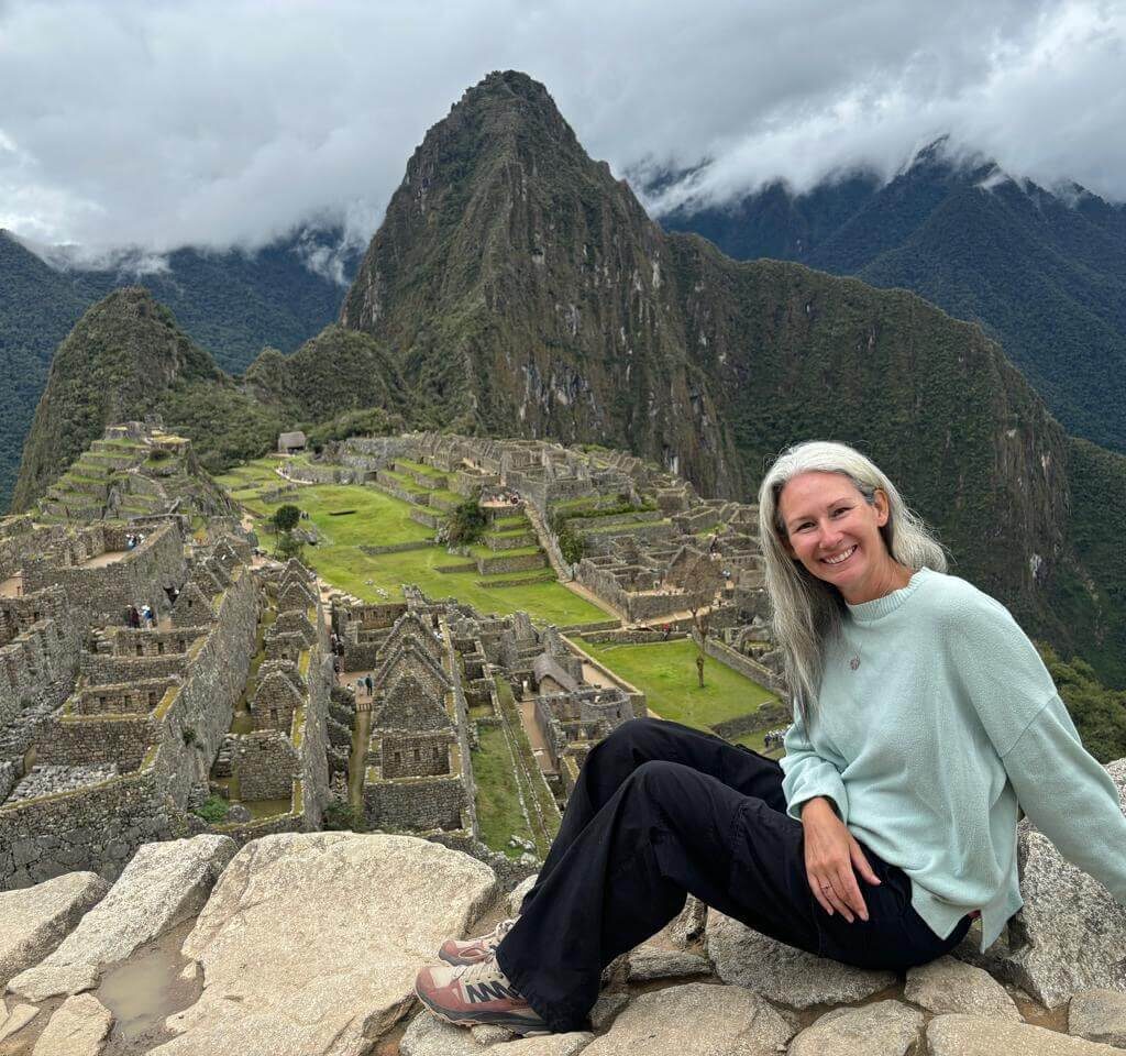 Traveler sitting on rock overlooking Machu Picchu ruins and Huayna Picchu mountain in October.