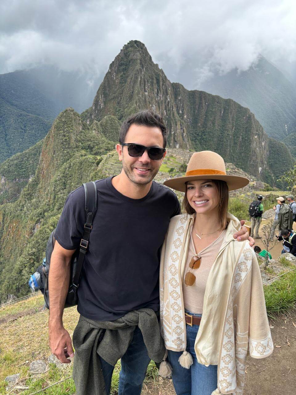 Couple posing at Machu Picchu viewpoint with Huayna Picchu mountain and cloudy October weather.