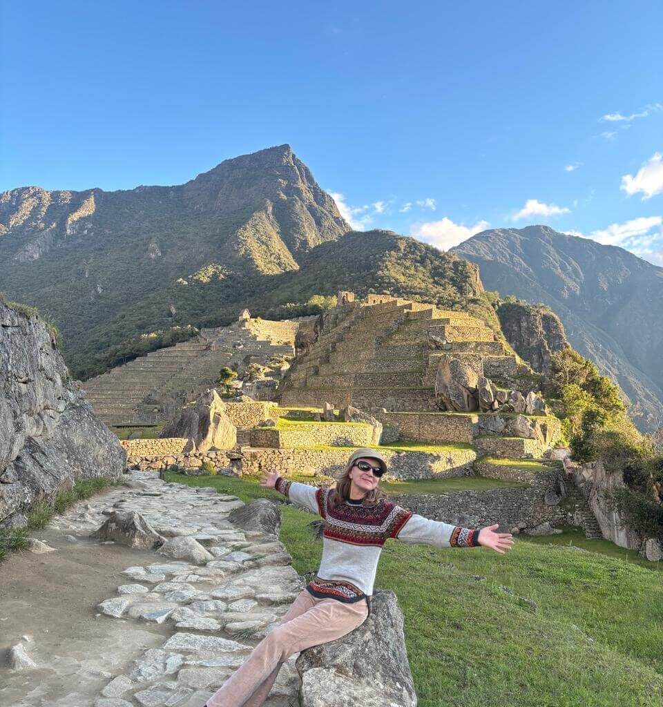Traveler sitting on stone near Machu Picchu terraces with warm sunset light in October.