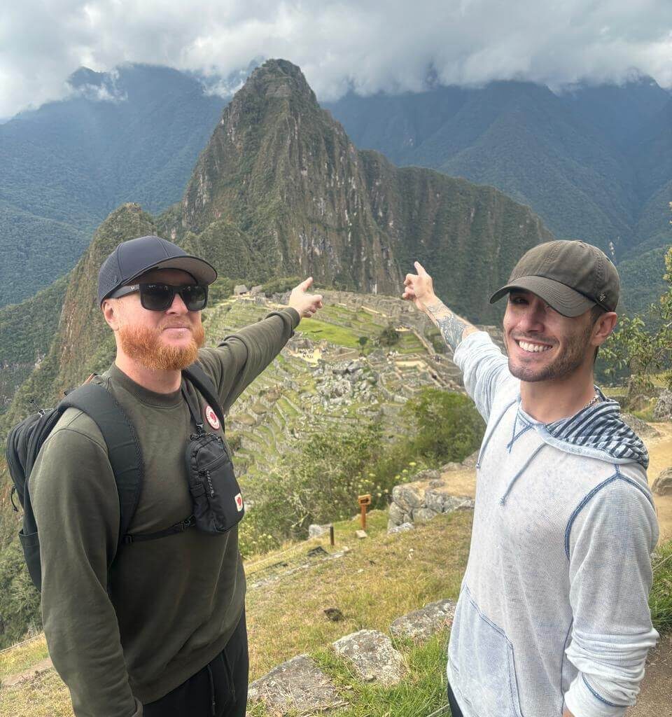 Two travelers pointing toward Huayna Picchu mountain above Machu Picchu ruins in October.
