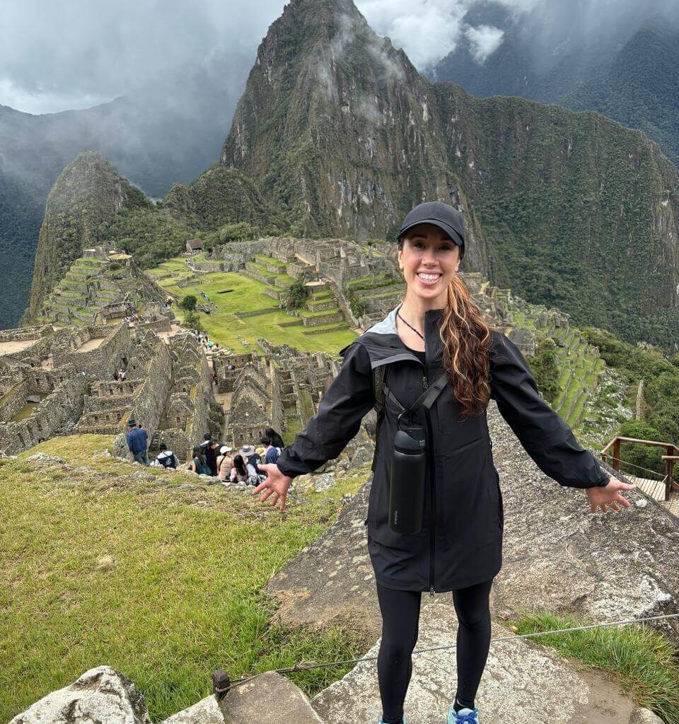 Female hiker standing above Machu Picchu ruins with Huayna Picchu mountain and clouds.