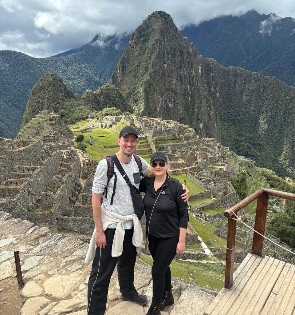 Couple posing at main Machu Picchu overlook with Huayna Picchu and terraces below.