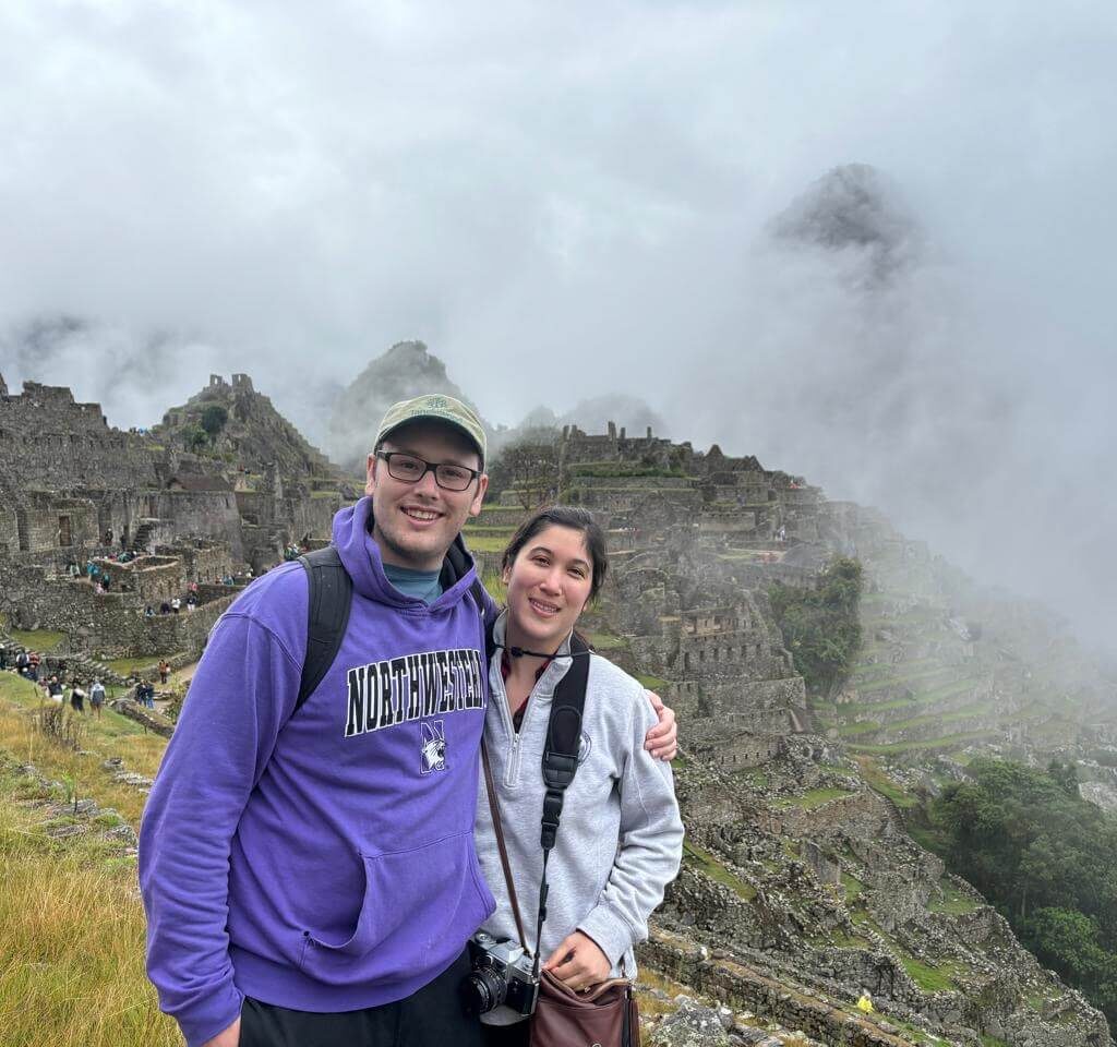 Travelers posing near Machu Picchu stone terraces with foggy October weather.