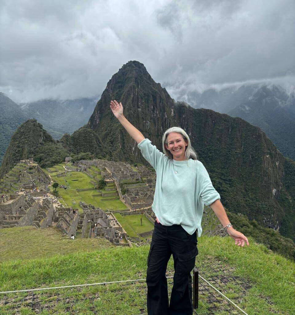 Woman standing at Machu Picchu viewpoint with terraces and mountains in October.