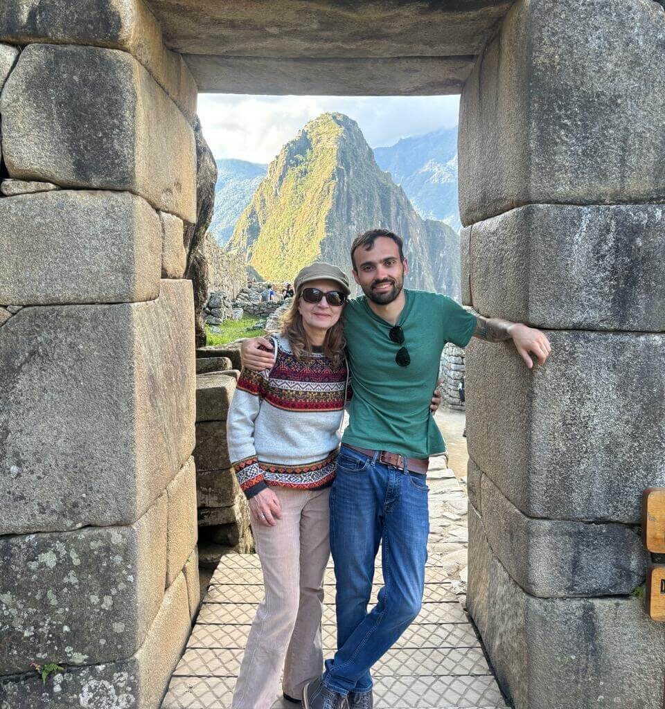 Two visitors standing in Machu Picchu stone doorway with Huayna Picchu mountain behind.