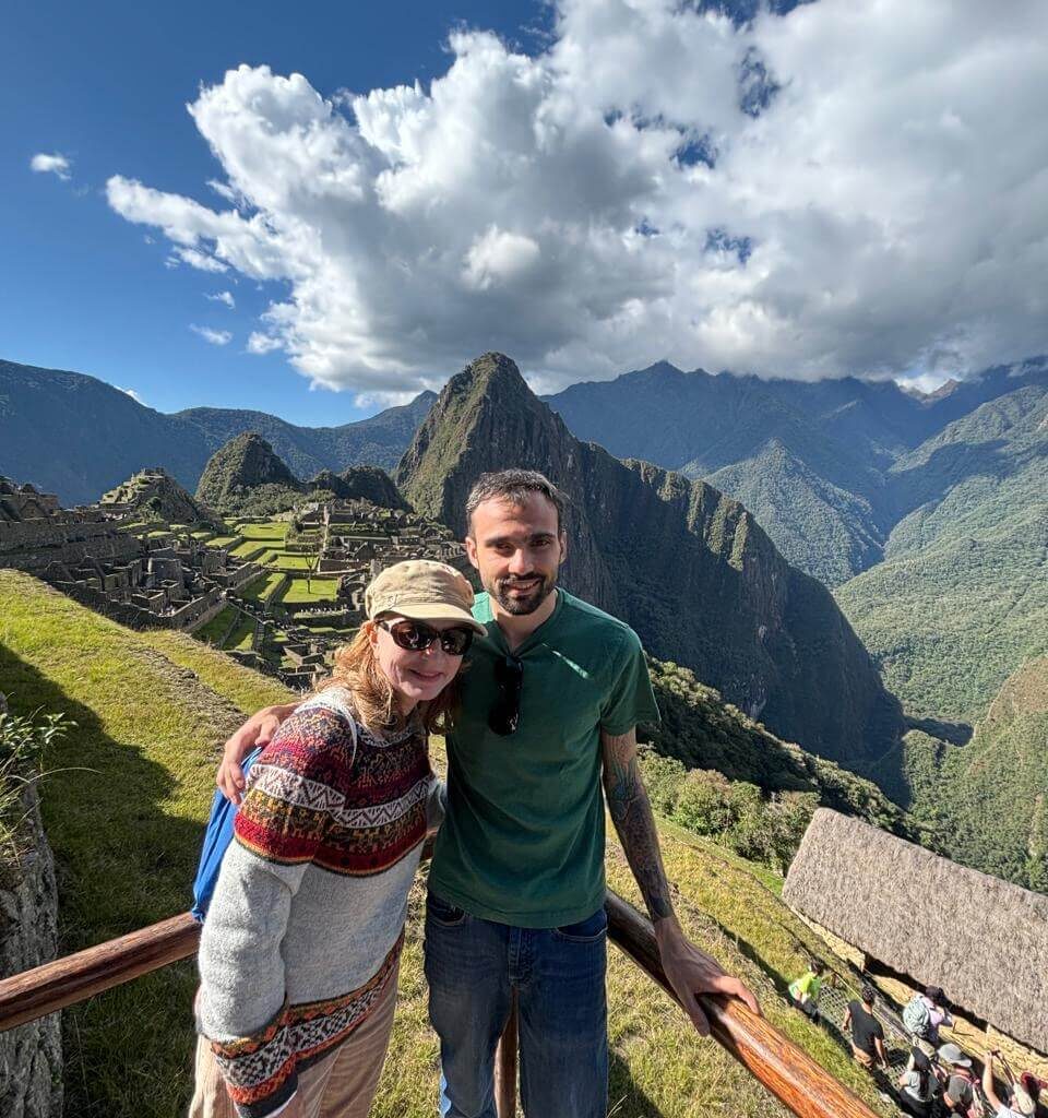 Couple standing at Machu Picchu viewpoint with blue sky and Andes mountains in October.