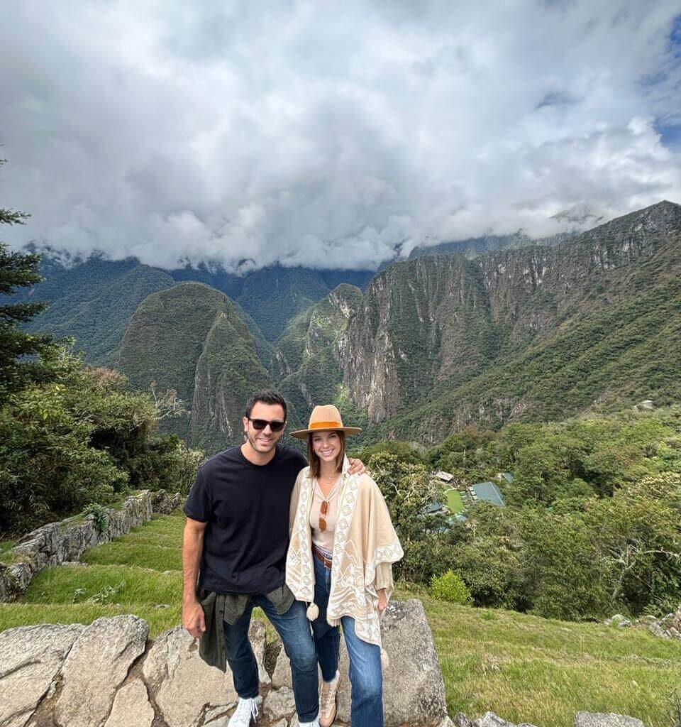 Couple standing on overlook with green mountains and cloudy October sky near Machu Picchu.