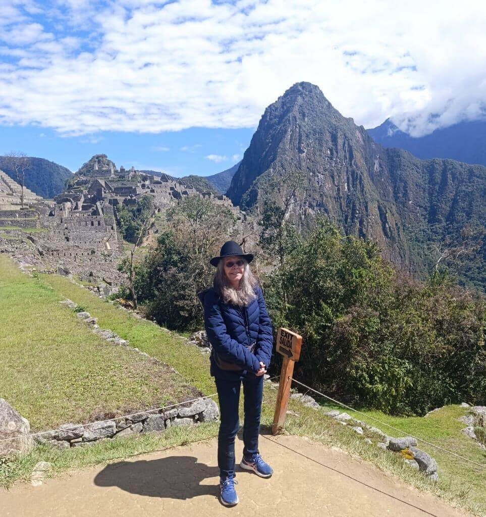Traveler standing near Machu Picchu ruins with blue sky and Andes mountains in September.