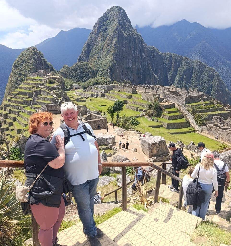 Travelers standing at railing overlooking Machu Picchu ruins and Huayna Picchu on a sunny September day.