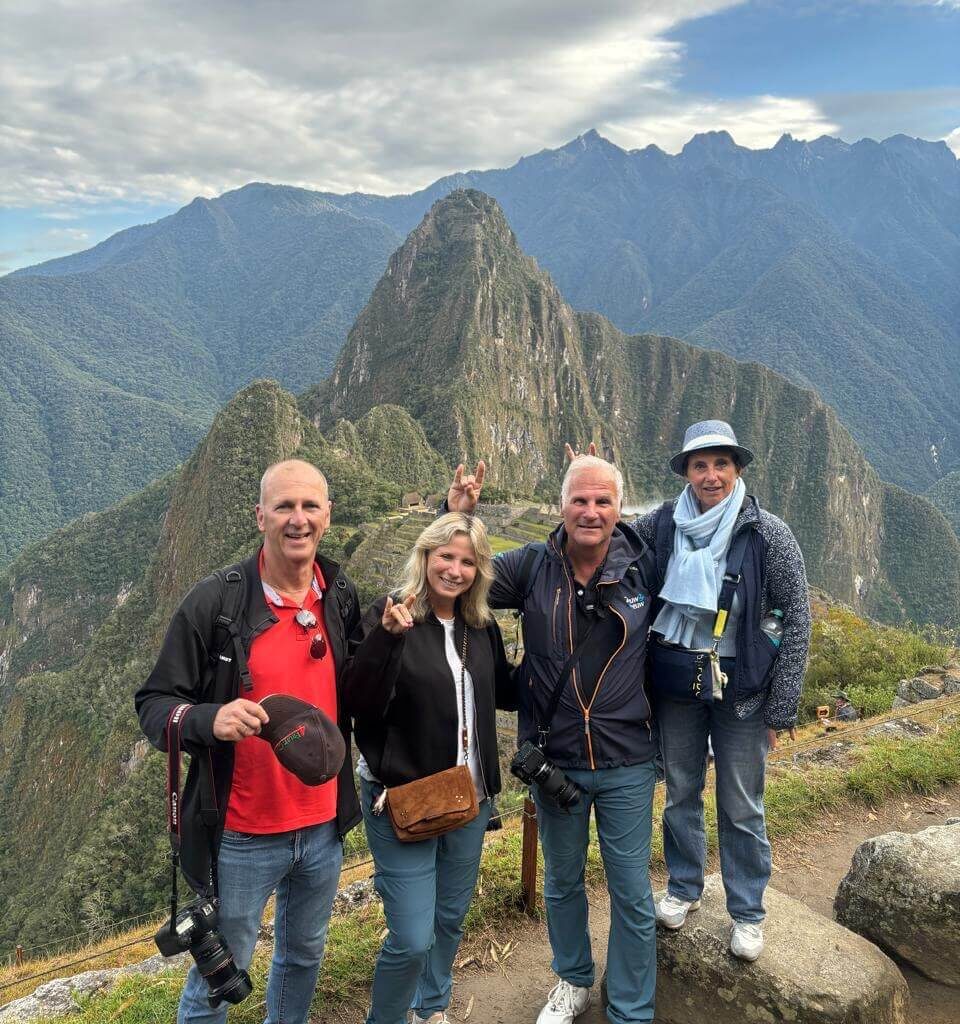 Four travelers posing with Huayna Picchu and Machu Picchu terraces in the Andes.