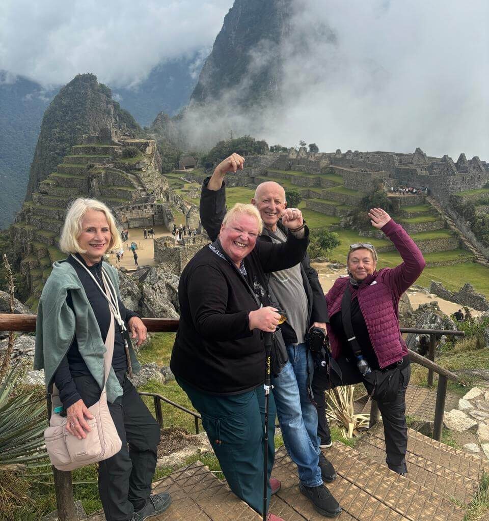 Group of travelers posing with Machu Picchu terraces and main ruins during cloudy September weather.