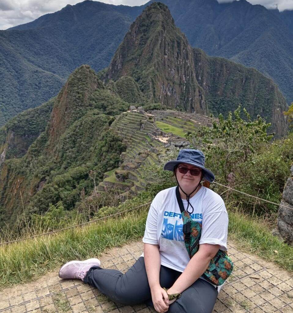 Traveler sitting at Machu Picchu viewpoint with terraces and green mountains behind.
